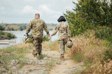 A man and a woman in the military uniform of Ukraine walk along the path and hold hands.