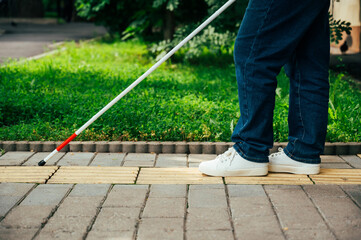 A blind woman walks outdoors using a cane along a tactile yellow tile.