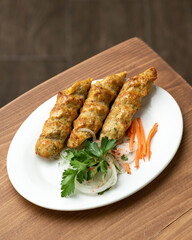 Three chicken kebabs with vegetables on white oval plate. Fried kebab with onions and carrots. Asian, Turkish cuisine. Fast food. Wooden background. Top view. Copy space.