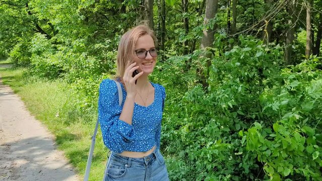 Beautiful Woman Is Walking In Green Park Smiling And Speaking By Smartphone. Slow Motion 4k Footage.