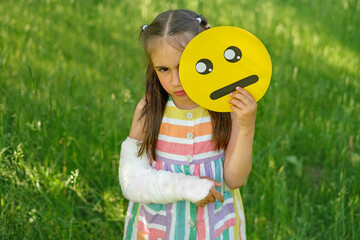 Sad girl with arm injury holds upset emoticon face.  Different faces of emojis displaying human emotions