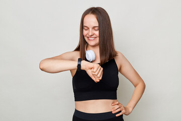 Sporty athletic woman wearing black top with headphones over neck standing isolated over white...