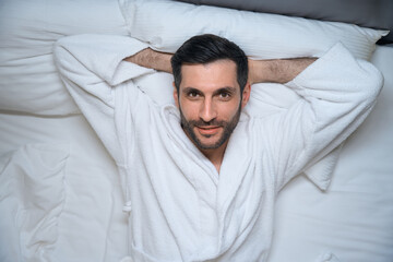 Satisfied rested man lies in bed in a hotel room