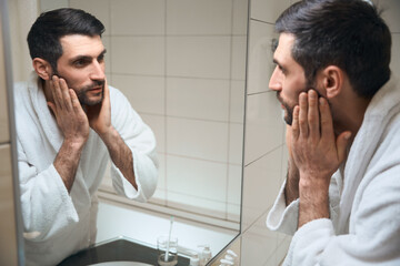 Middle-aged man looks in the mirror in the bathroom