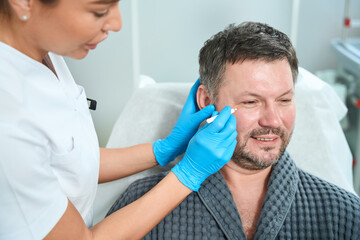 Health worker at consultation examines the face of middle-aged patient