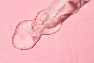 Dropper pipette with transparent liquid and bubbles drops on pink background, beauty and skin care...
