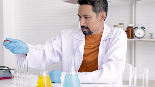 Professional scientist with beard drop liquid blue and yellow solution, teacher analyzed experimental results in science room, medical science test tube with chemical fluid testin in laboratory lab.