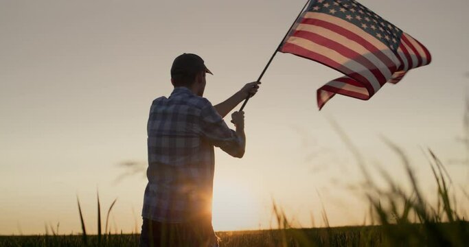 Silhouette of a young man waving the American flag. Standing in a field of wheat at sunset