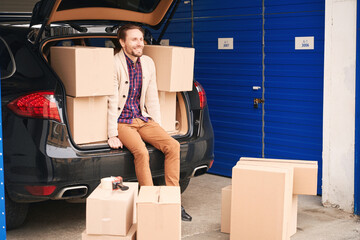 Happy man with cardboard boxes in car trunk at storage warehouse © Viacheslav Yakobchuk