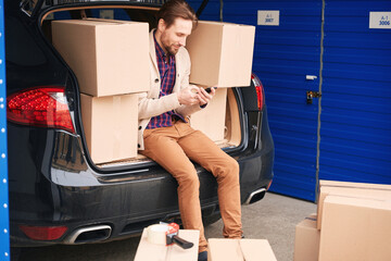 Guy with cardboard boxes in car trunk into warehouse with self-storage unit