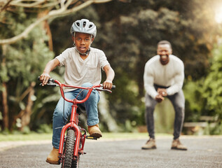Boy on bicycle, father cheers and learning cycling with help, helmet for safety and family in park. Support, motivation and trust, black man and young kid outdoor, teaching and learn bike riding