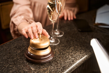 Female hand ringing golden bell for service at counter desk in the bar