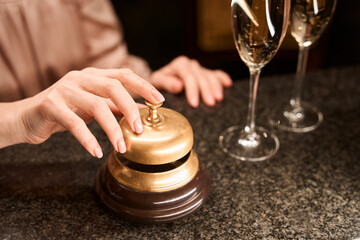 Female hand ringing golden service bell at counter desk in the bar