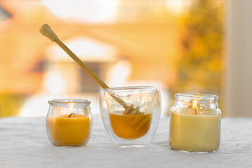 Composition on the theme of honey massage. On a white towel there is a glass of liquid honey and a honey stick, next to candles 