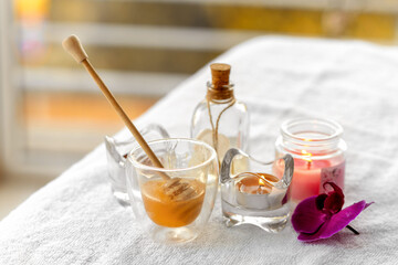 Composition on the theme of honey massage. On a white towel there is a glass of liquid honey and a...