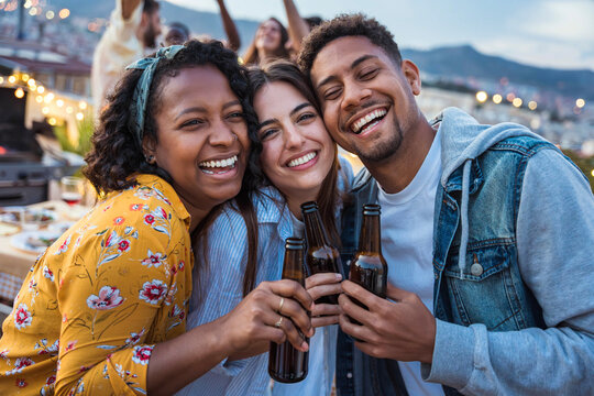 Multiethnic friends toasting beer at rooftop summer party - Group of diverse young people having dining time together at restaurant balcony - Life style concept with guys and girls hanging together