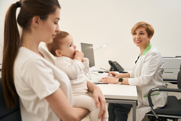 Fototapeta premium Friendly female pediatrician receiving parent with child in her office