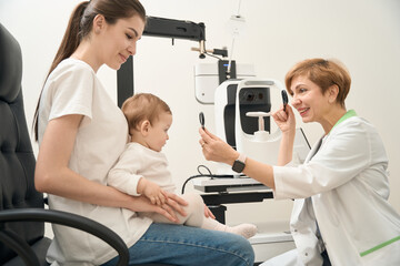Friendly ophthalmologist checking child ocular health in presence of mother