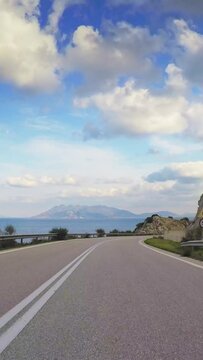 POV car traveling, sea, clouds in the sky, curvy road and rocky cut slope, vertical footage