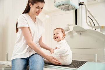 Obraz premium Smiling woman preparing toddler for digital x-ray