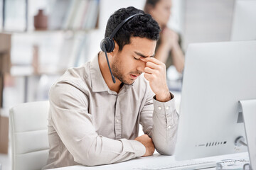 Mental health, man with headache and headset at his desk with computer in a modern workplace...