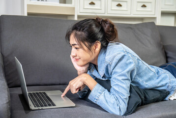 Asian woman is resting on the sofa in her own house, chatting on a video call with a close female friend on the computer laptop screen, Working from home