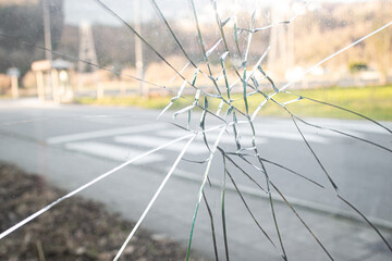 A glass window of a car punched by an angry people who hits a punch, a blurry background of a street with road and grass on a summer day 