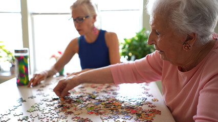 Two happy elderly mature women talking and playing with puzzle pieces.