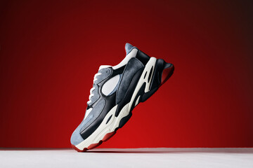 Modern sneakers with leather accent on red background. Trainers on big sole. Urban fashion...