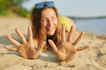 Happy girl with hands in the sand on the beach.Hands with grains of sand. The concept of summer holidays. - obrazy, fototapety, plakaty