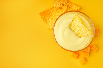 Bowl with tasty cheddar cheese sauce and nachos on yellow background