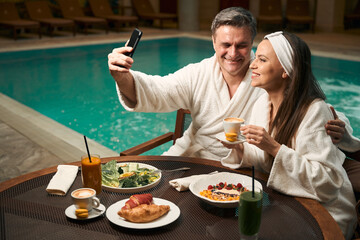 Romantic mature couple taking selfies with smartphone at spa resort