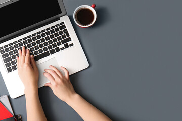 Female programmer using laptop with cup of coffee on dark background