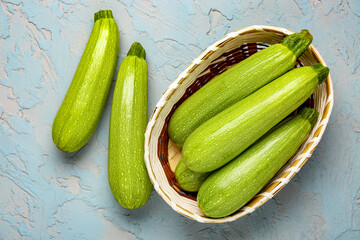 Wicker bowl with many fresh green zucchini on blue background