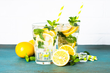 Lemonade in glass on white table with fresh lemons and mint. Cold summer drink.