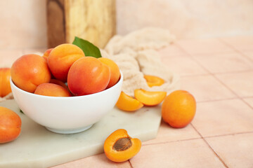 Board with bowl of fresh apricots on pink tile table