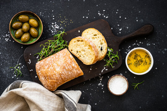 Ciabatta bread with olive oil, olives and herbs on black. Mediterranean food. Top view.