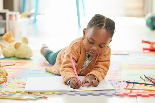 Black girl, floor and learning with art education, drawing and color to relax, happiness and writing. Female kid, toddler and young person on the ground, home and child development with happiness