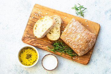 Italian ciabatta bread on wooden board with olive oil and herbs. Top view on white background.