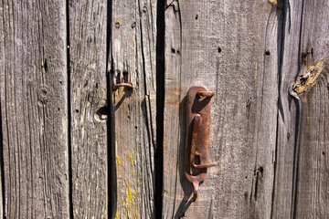 An old, original doorknob on a centuries-old wooden barn door in the harsh afternoon sun. Day. - 609412526