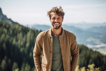 Handsome young man standing on top of a mountain and smiling