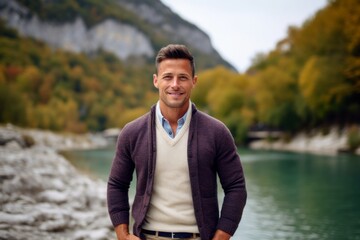 Naklejka na ściany i meble Handsome man on the background of the river and mountains in autumn