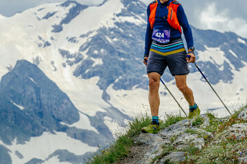 man athlete walk skyrunning marathon trail race in background snowy mountain, trekking poles in hands