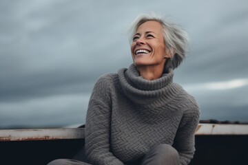 Fototapeta na wymiar Portrait of happy senior woman in grey sweater against cloudy sky.