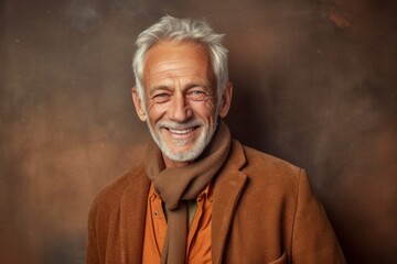Smiling senior man with grey hair wearing a brown coat and scarf.