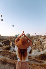 Young woman  stands on the mountain with flying air balloons on the background.  Famous tourist...