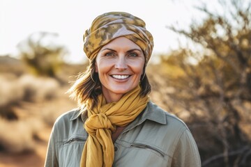 Portrait of smiling mature woman in hat and scarf standing in desert