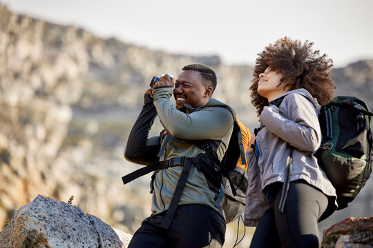 Hiking, camera and photographer with couple in mountains for journey, climbing and travel. Relax, trekking and adventure with black man and woman hiker in nature for exercise, picture and motivation