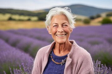 Fototapeta na wymiar Portrait of happy senior woman standing in lavender field and smiling