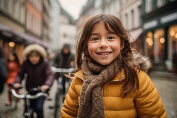 Portrait of a smiling little girl in a yellow coat with a bicycle in the city